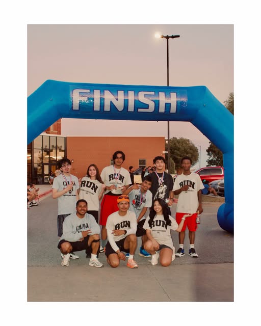 The crew smiling together beneath a blue finish arch